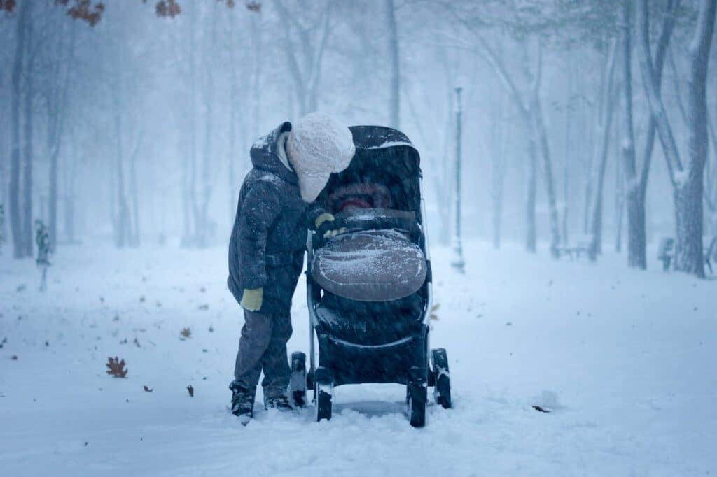 A child looking into a baby buggy on a snowy road